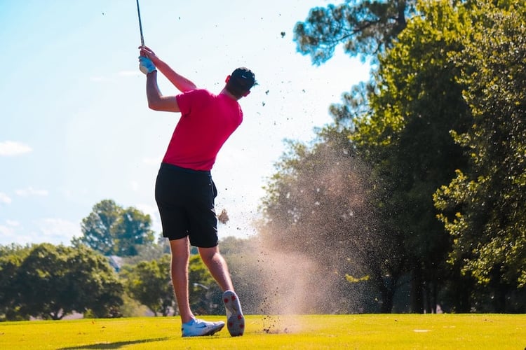 golfer swinging club trees grass green blue sky golf